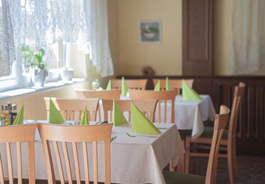 Gedeckter Tisch in einem Gasthaus, Holztisch mit weißer Tischdecke und grünen Servietten