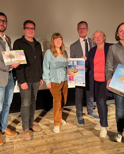 Pressefoto vor der Leinwand des Kinos Mistelbach, bei der Präsentation von Rettet das Dorf. Vertreter:innen halten Werbematerial in die Kamera