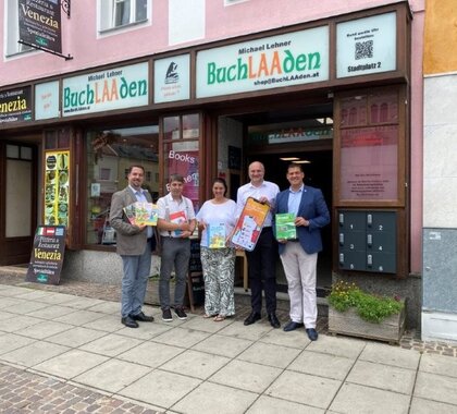 Am Bild zu sehen die Vertreter der Projektträger Städte vor einem Buchladen mit dem Werbesujet Plakat zur Cities-App