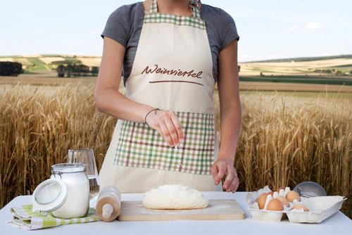 Frau in Schürze steht in einem Feld an einem Tisch und bereitet ein Weinviertlerbrot vor. Das Foto ist bis zu ihrem Hals aufgenommen