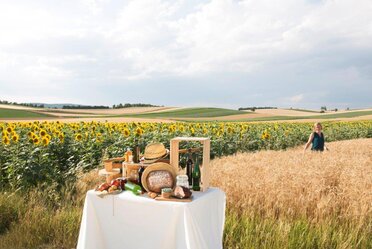 Gedeckter Tisch mit Weinviertel Produkten vor einem Sonnenblumenfeld und einem Getreidefeld, Mensch steht im Hintergrudn