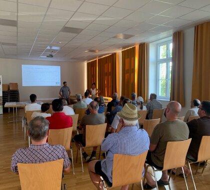 Bei der Infoveranstaltung zur Kellergassen Schutzzone Wildendürnbach Präsentiert der Raumplaner , davor sitzen rund 20 Personen auf Stühlen und hören dem Vortrag zu.