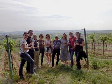 Eine Gruppe von jungen Personen steht im Weingarten zu einem Gruppenbild zusammen. Es ist Frühling und der Weingarten beginnt seine Blätter auszutreiben.