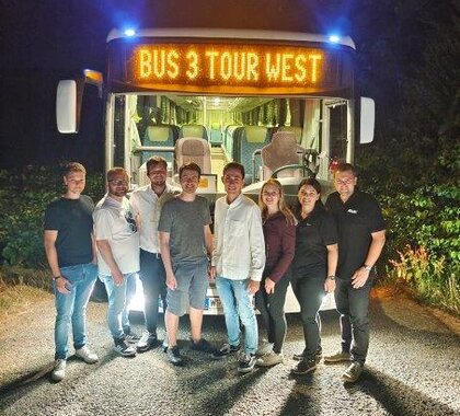 Jugendliche vor einem beleuchteten Bus auf dem Weg zum Jugendfestl SanDsation, im Hintergrund Nachthimmel