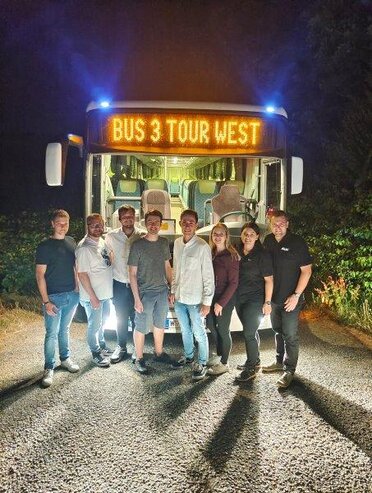 Jugendliche vor einem beleuchteten Bus auf dem Weg zum Jugendfestl SanDsation, im Hintergrund Nachthimmel