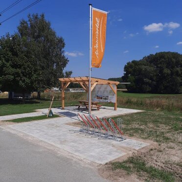 Der Weinviertel-Rastplatz in der Gemeinde Wilfersdorf. Im Vordergrund steht eine Weinviertel-Fahne, dahinter eine Pergula mit einer Sitzmöglichkeit.