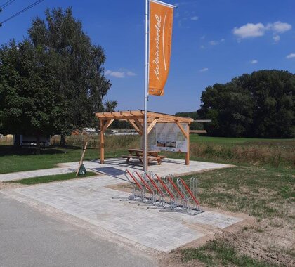 Der Weinviertel-Rastplatz in der Gemeinde Wilfersdorf. Im Vordergrund steht eine Weinviertel-Fahne, dahinter eine Pergula mit einer Sitzmöglichkeit.