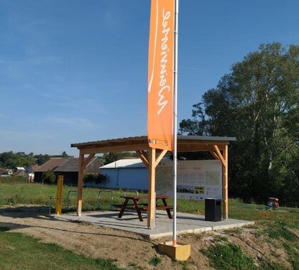 Ein Weinviertel Radrastplatz in der Landschaft mit einer Holzpergola und einer orangenen Weinviertel Fahne davor.