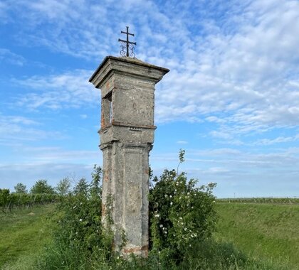 Weißes Marterl auf einem Feld im Grünen.