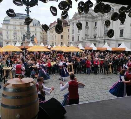 Dreitagesfest am Wiener Hof, von einer Bühne wird auf den Platz fotografiert. Im Hintergrund sind Biergarnituren auf denen viele Menschen feiern mit Weinviertel Sonnenschirmen zu sehen.