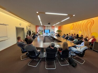 Präsentation der Ergebnisse der Sozialraumanalyse im südlichen Weinviertel. 26 Personen sitzen an einem Arbeitstisch, am Bildschirm sind Ergebnisse der Studie zu sehen.