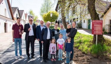 Mehrere Erwachsene, unter anderem Landtagspräsident Wilfing sowie Bürgermeister Richter, und Kinder stehen gemeinsam in einer Weinviertler Kellergasse in Falkenstein. Hinter ihnen sind typische Presshäuser mit weißen Fassaden zu sehen, daneben steht eine Informationstafel zur romantischsten Kellergasse Falkensteins.