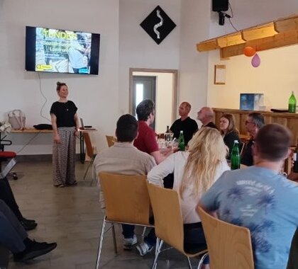 Eine Dame präsentiert die Ergebnisse der Sozialraumanalyse, am Bildschirm im Hintergrund ist die Studie zu sehen. Im Vordergrund sitzen Personen an Tischen mit dem Blick auf den Bildschirm gerichtet.