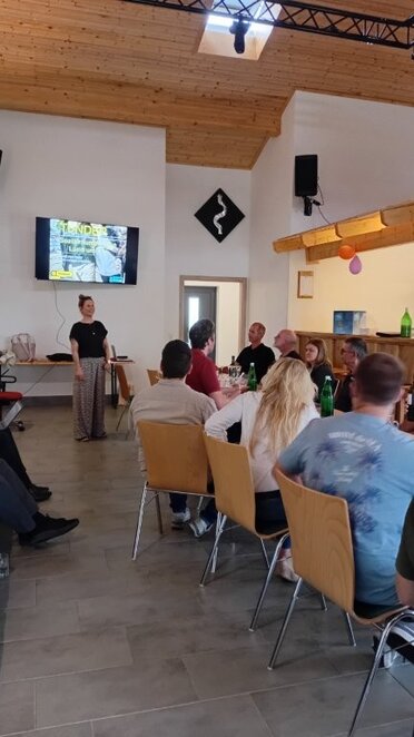 Präsentation Sozialraumanalyse Land um Laa, C: Lebensraum Land um Laa Eine Dame präsentiert die Ergebnisse der Sozialraumanalyse, am Bildschirm im Hintergrund ist die Studie zu sehen. Im Vordergrund sitzen Personen an Tischen mit dem Blick auf den Bildschirm gerichtet.