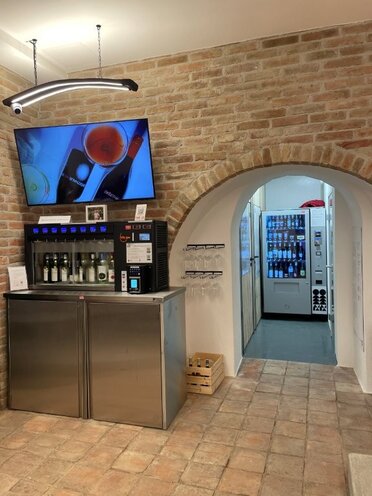 Im inneren des Presshauses steht ein Automat zur glasweisen Weinverkostung. Darüber hängt ein Bildschirm auf dem Videos mit Informationen zu Weinen zu sehen ist.
