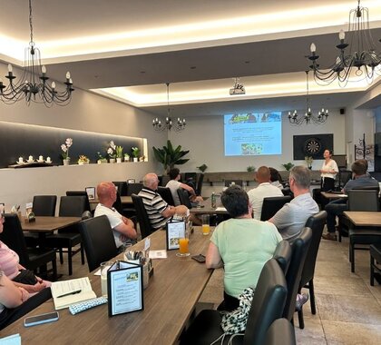 Eine Dame präsentiert die Ergebnisse der Sozialraumanalyse, an der Leinwand im Hintergrund ist die Studie zu sehen. Im Vordergrund sitzen Personen an Tischen mit dem Blick auf die Leinwand gerichtet.