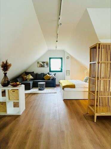 Der Nächtigungskeller von innen, Wohnbereich mit Holzboden, schräge Dachgeschosswände mit Sitzecke sowie Bett und Raumteiler