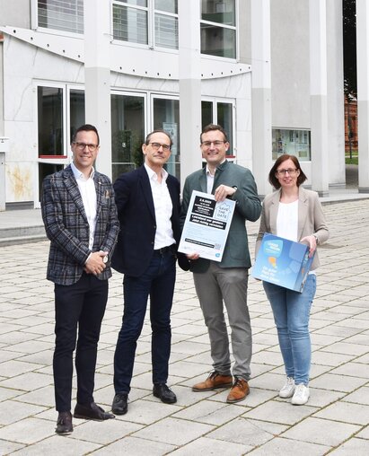 Gruppenfoto, vier Personen mit Plakat vor Stadtsaal Mistelbach