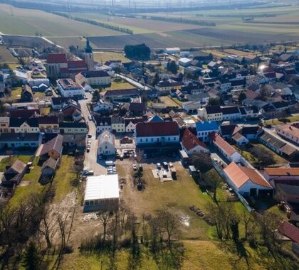 Luftaufnahme des Ortes Pillichsdorf. Im Vordergrund ist die Gemeindewiese mit dem Gasthaus zu sehen, im Hintergrund die Kirche.