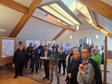 Diskussion Teilbebauungspläne Kellergassen Schutzzone Pillichsdorf, C: Marktgemeinde Pillichsdorf Diskussionsformat in Pillichsdorf zum neuen Teilbebauungsplan. Viele Bewohner:innen stehen im Gemeindesaal mit dem Blick richtung Präsentationsfläche. Am Rand stehen Pinnwände auf denen Pläne aufgehängt sind.