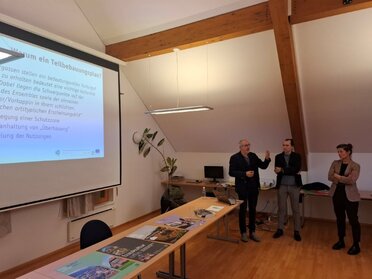 Diskussion Teilbebauungspläne Kellergassen Schutzzone Pillichsdorf, C: Marktgemeinde Pillichsdorf Drei Personen präsentieren Informationen zur Kellergassen-Schutzzone in Pillichsdorf auf deiner Power Point Präsentation, ihr Blick ist auf die Leinwand gerichtet.