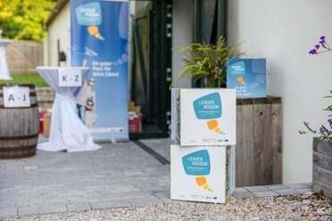 Im Vordergrund stehen LEADER-Werbewürfel im neuen Corporade Design, im Hintergrund ist das Roll up im neuen Design zu sehen.