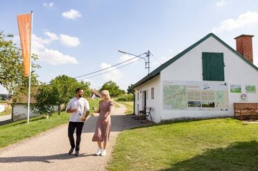Ein junges Pärchen spaziert durch eine Kellergasse bei einem Genussrastplatz in einem Keller, im Hintergrund ist eine Weinviertelfahne zu sehen.