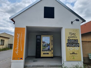 Genussrastplatz Großkrut, ein weißer Keller mit einem orangen Weinviertel Schild im Eingangsbereich und einem Getränkeautomaten im Innenbereich.