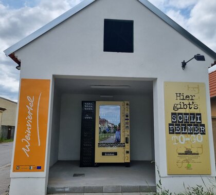 Genussrastplatz Großkrut, ein weißer Keller mit einem orangen Weinviertel Schild im Eingangsbereich und einem Getränkeautomaten im Innenbereich.