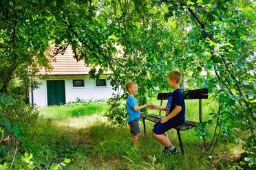 Kellerviertel in Prottes, im Hintergrund ist ein weiß gefärbter Keller zu sehen, im Vordergrund ein Laubbaum unter dem zwei Kinder auf einer Holzbank sitzen. 