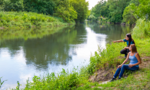 Menschen sitzen an einem Fluss im Grünen und schauen darauf